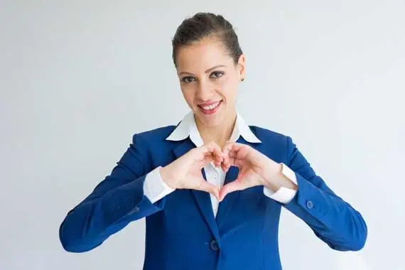 Femme en veston bleu formant un cœur avec ses mains, regard souriant vers la caméra